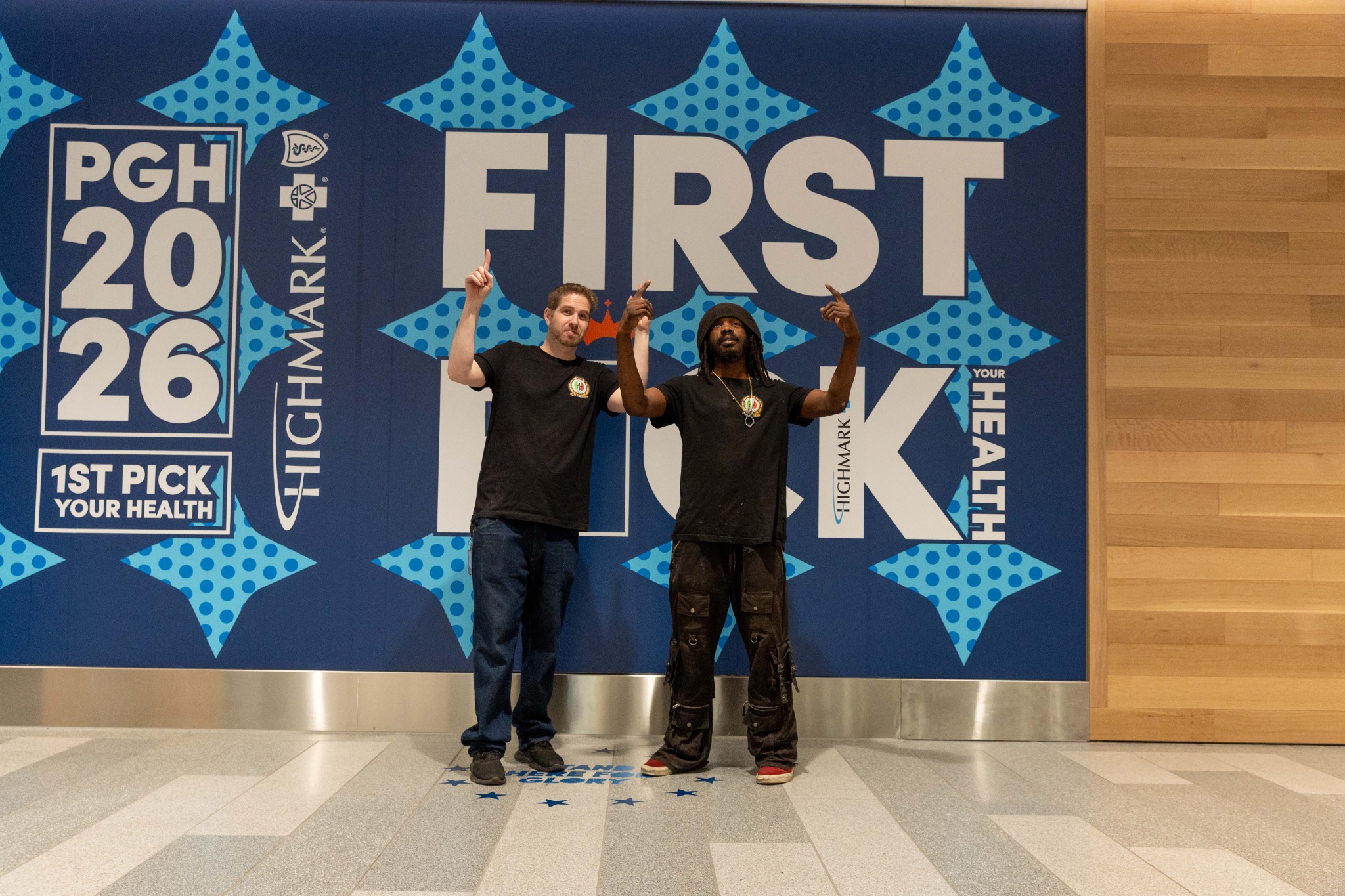 Two fans posing at the First Pick Your Health wall